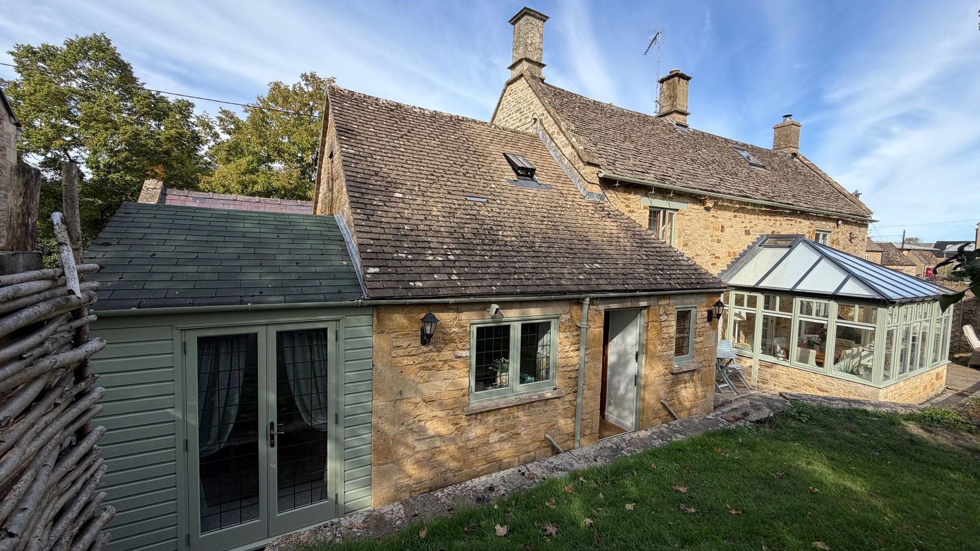 Rear of Glebe Cottage with the Breakfast Room French doors and conservatory in autumn sunshine, Bledington